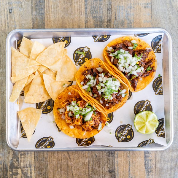 Three Diablos Tacos with tortilla chips and a lime wedge on a metal tray.