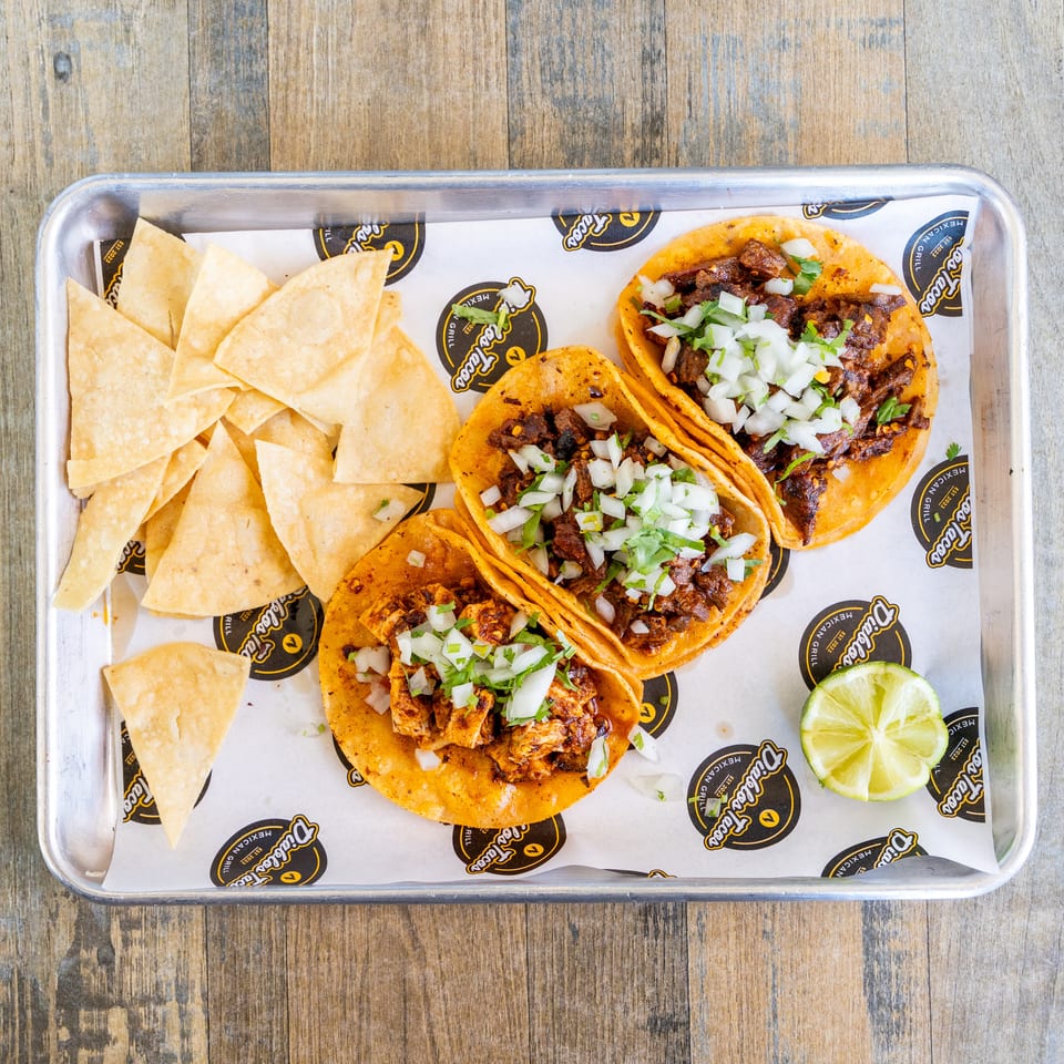 Three Diablos Tacos with tortilla chips and a lime wedge on a metal tray.