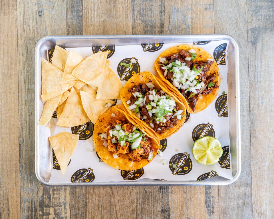 Three Diablos Tacos with tortilla chips and a lime wedge on a metal tray.