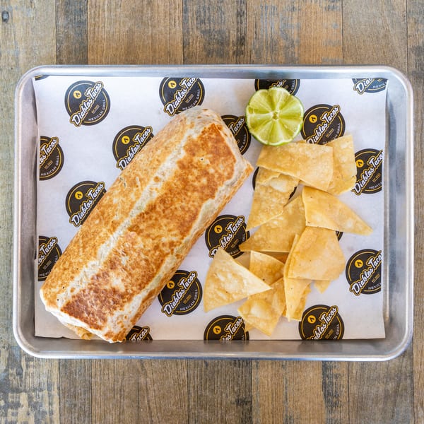 A Diablos Tacos burrito, tortilla chips, and a lime wedge on a metal tray.