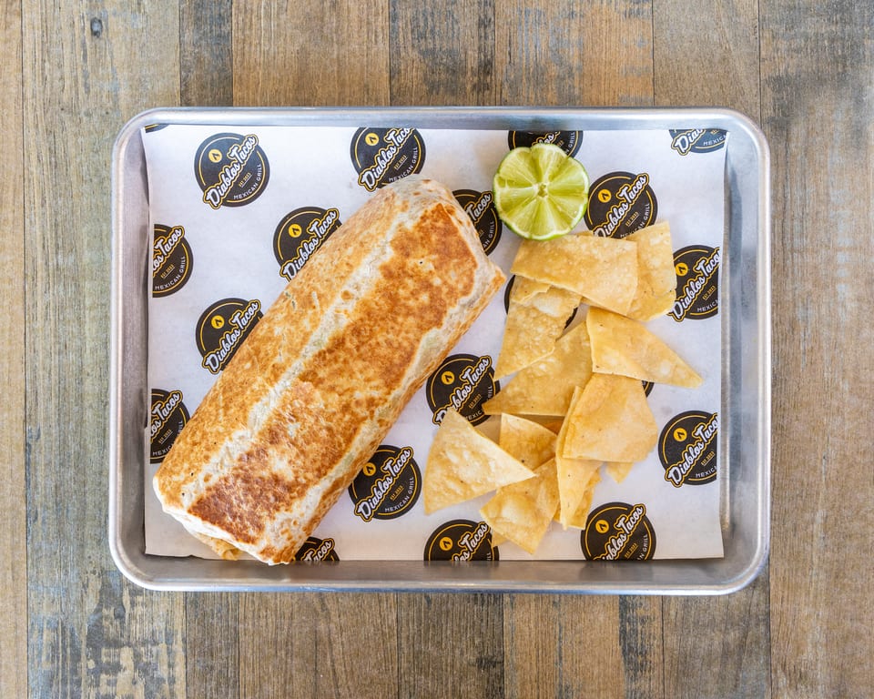 A Diablos Tacos burrito, tortilla chips, and a lime wedge on a metal tray.