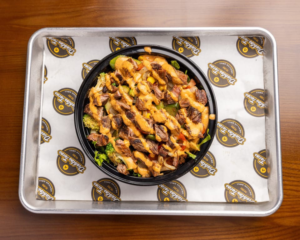 Diablos Tacos steak bowl with broccoli, corn, and peppers, drizzled with sauce on a branded tray.