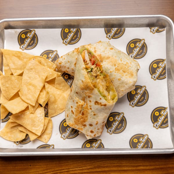 A Diablos Tacos burrito, cut in half to show the filling, with tortilla chips on a tray.