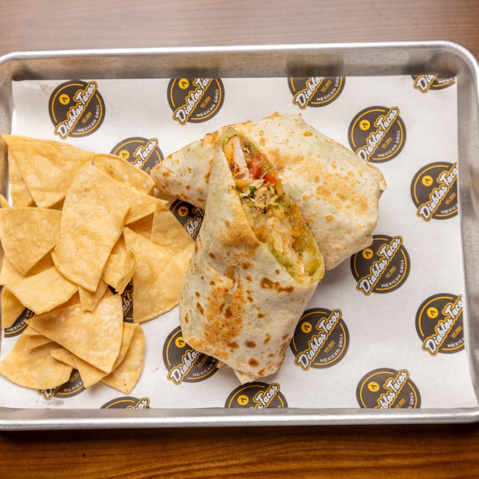A Diablos Tacos burrito, cut in half to show the filling, with a side of tortilla chips.