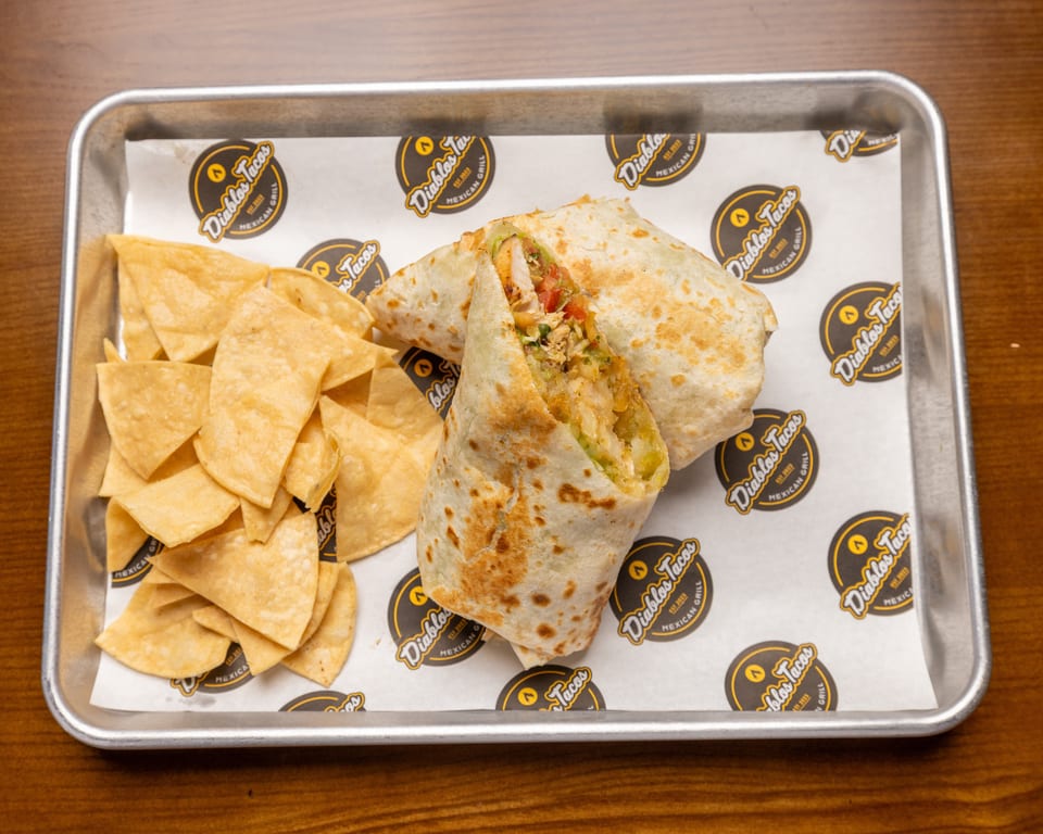 A Diablos Tacos burrito, cut in half to show the filling, with a side of tortilla chips.