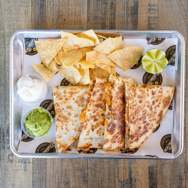 A tray of Diablos Tacos quesadillas, tortilla chips, guacamole, sour cream, and a lime wedge.