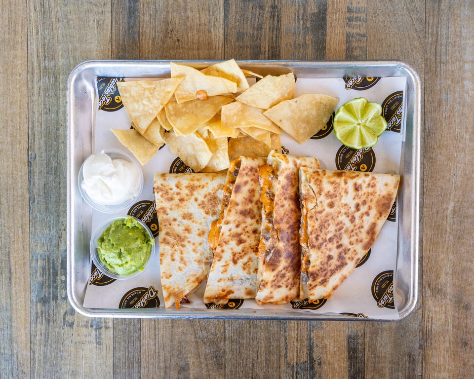A tray of Diablos Tacos quesadillas, tortilla chips, guacamole, sour cream, and a lime wedge.