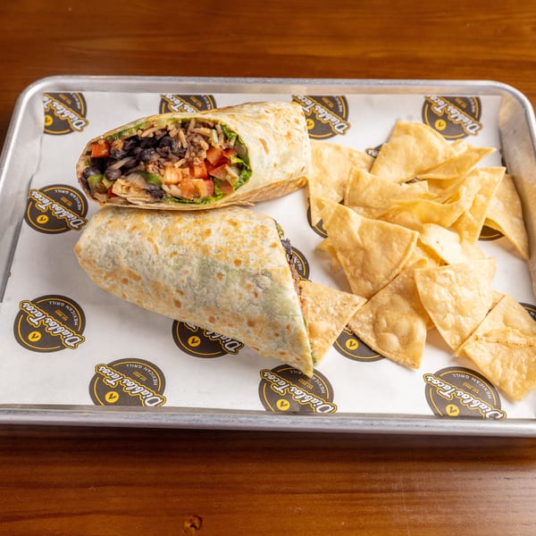 Two burritos, one cut open to show rice, beans, and vegetables, with tortilla chips on a tray.