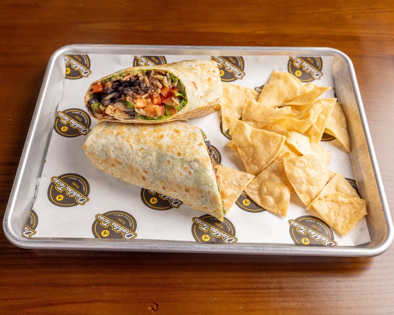 Two burritos, one cut open to show rice, beans, and vegetables, with tortilla chips on a tray.